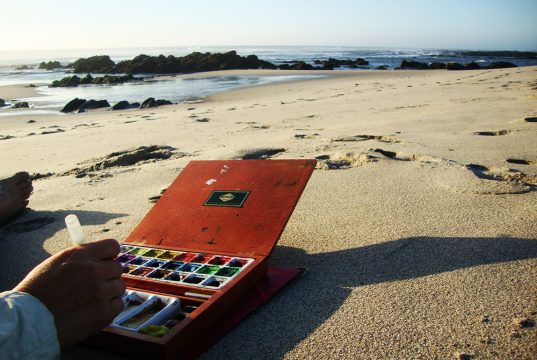 Palette d'aquarelle posée sur le sable au bord de l'océan au Portugal