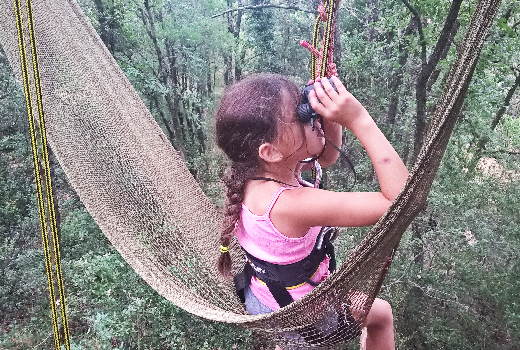 petite fille observant aux jumelles dans un hamac suspendu dans les arbres